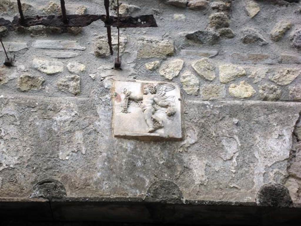 III.3 Herculaneum. June 2011. Marble relief of cupid on wall above the pool.
Photo courtesy of Sera Baker.